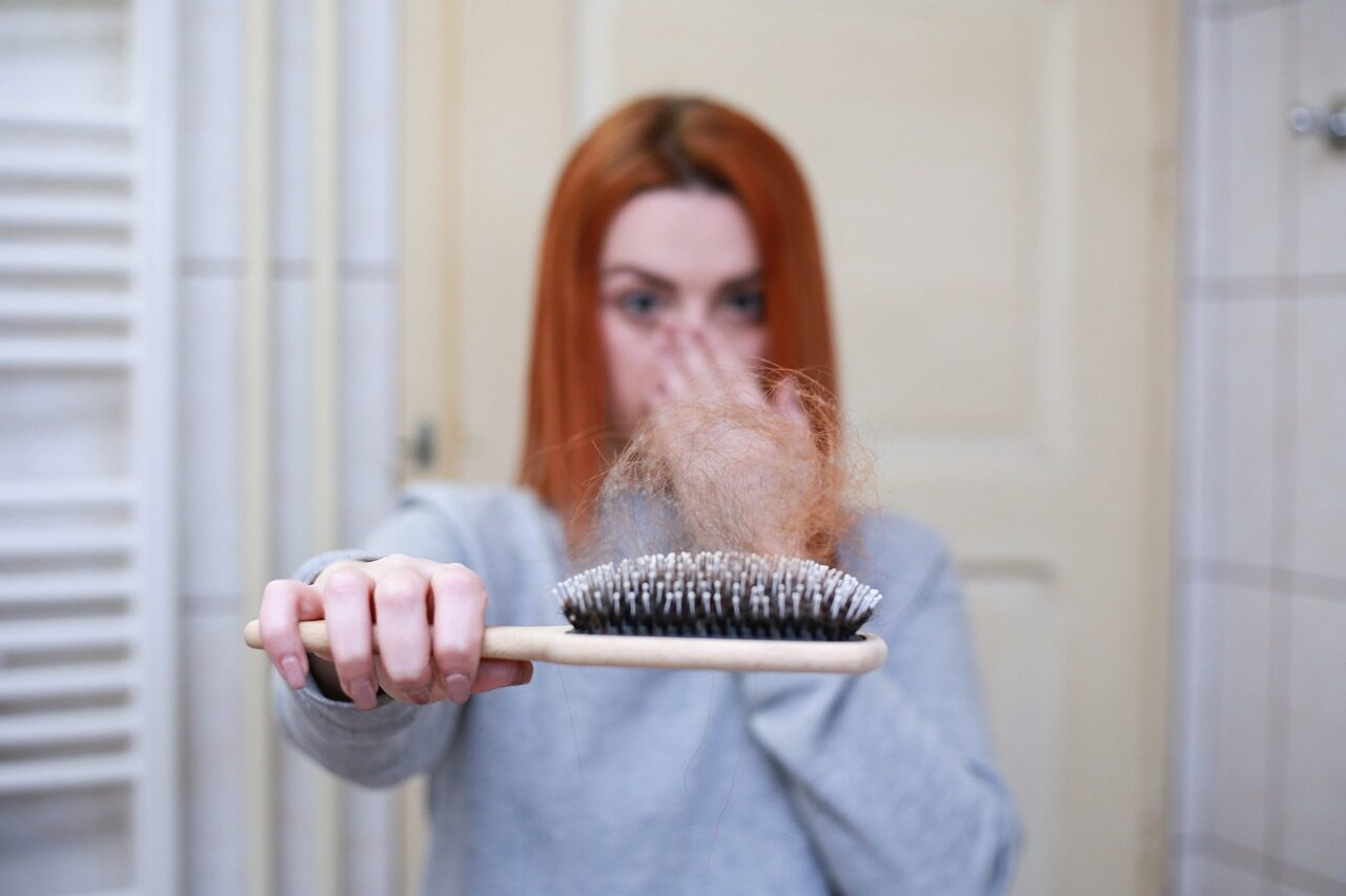 mulher com fios de cabelo na escova para ilustrar pauta de como diminuir a queda de cabelo