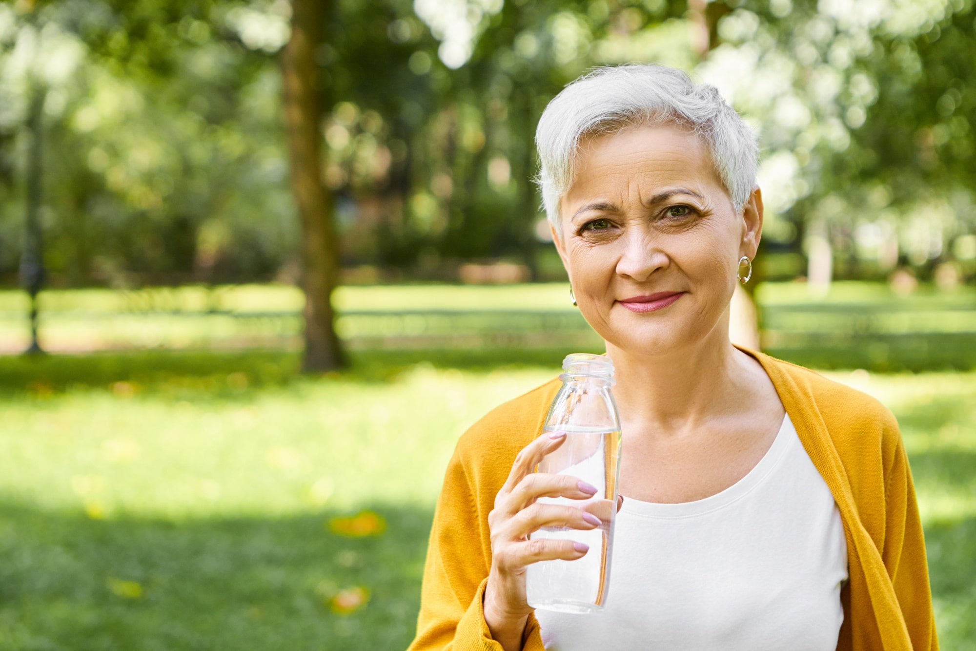 mulher de cabelos grisalhos em um parque com garrafa de água na mão