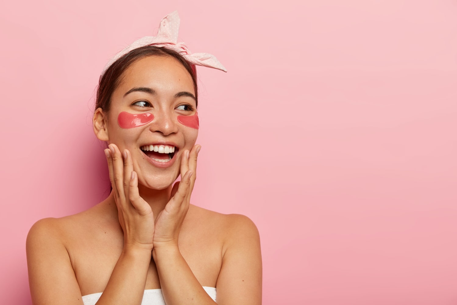 mulher asiática com faixa na cabeça e máscara abaixo dos olhos e mãos no rosto com expressão de felicidade