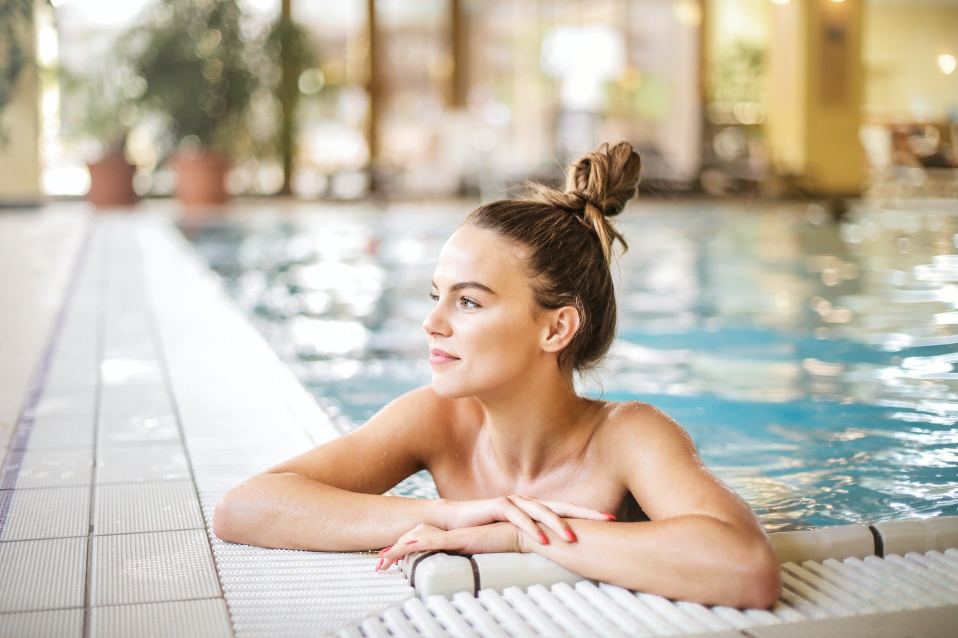 mulher na borda da piscina com um coque no cabelo olhando para o lado