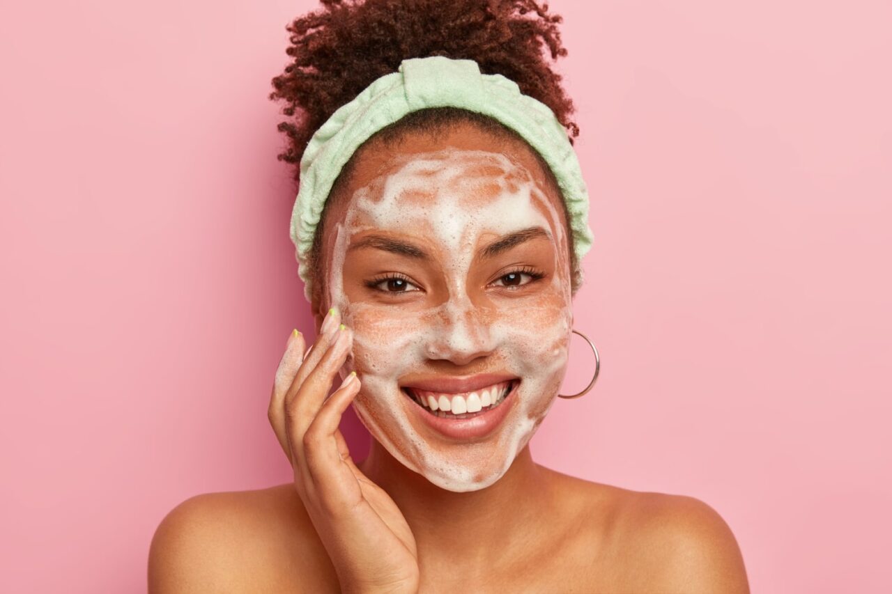 mulher com sabão no rosto para ilustrar texto sobre como preparar a pele para maquiagem