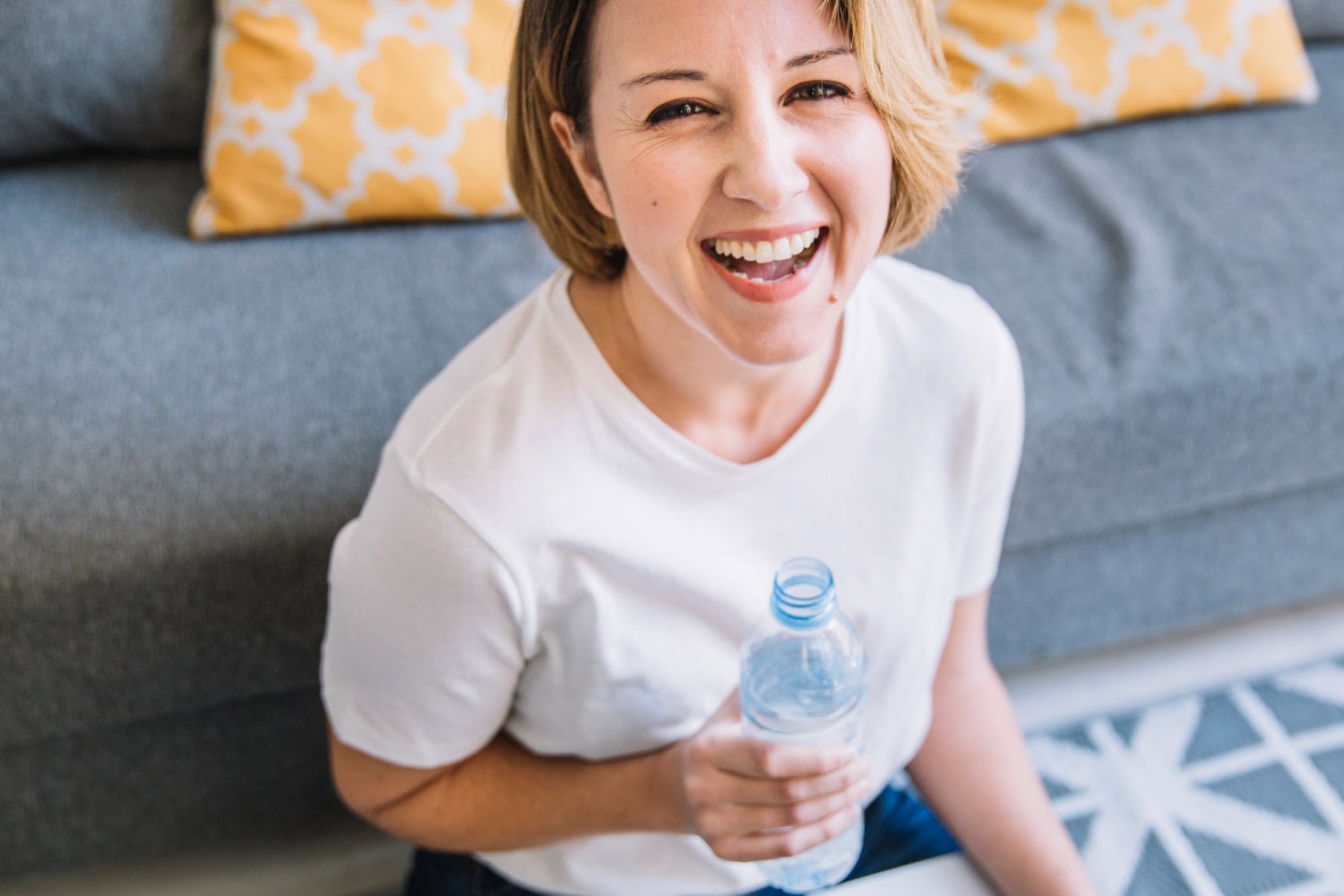 mulher sorrindo e bebendo água para ilustrar texto sobre benefícios da água para a pele
