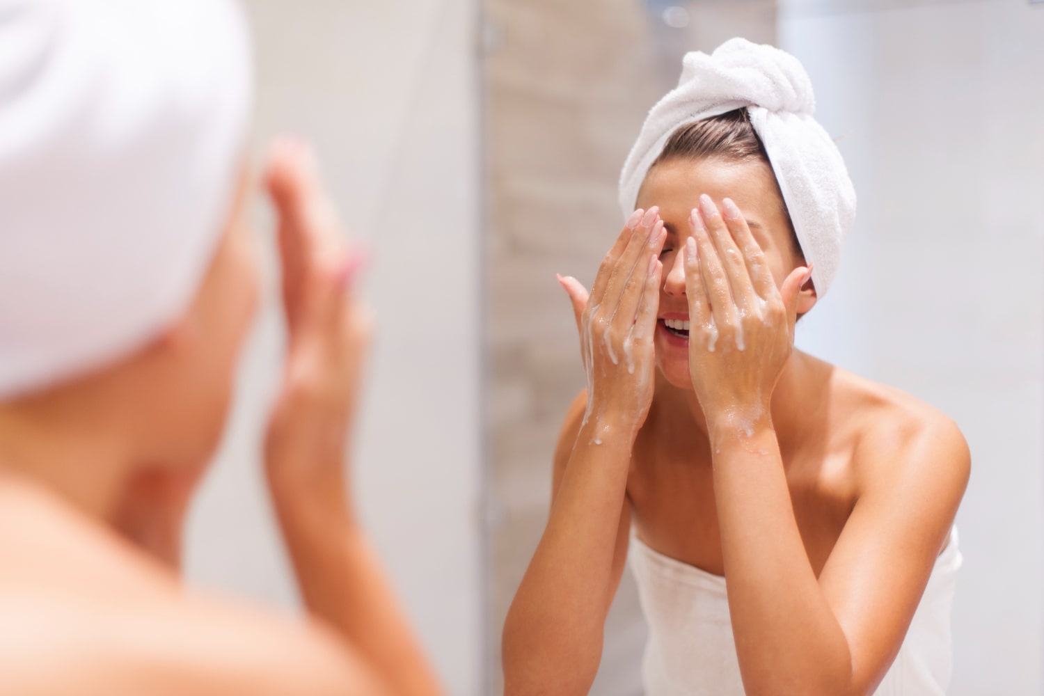 mulher com toalha na cabeça lavando o rosto no banheiro